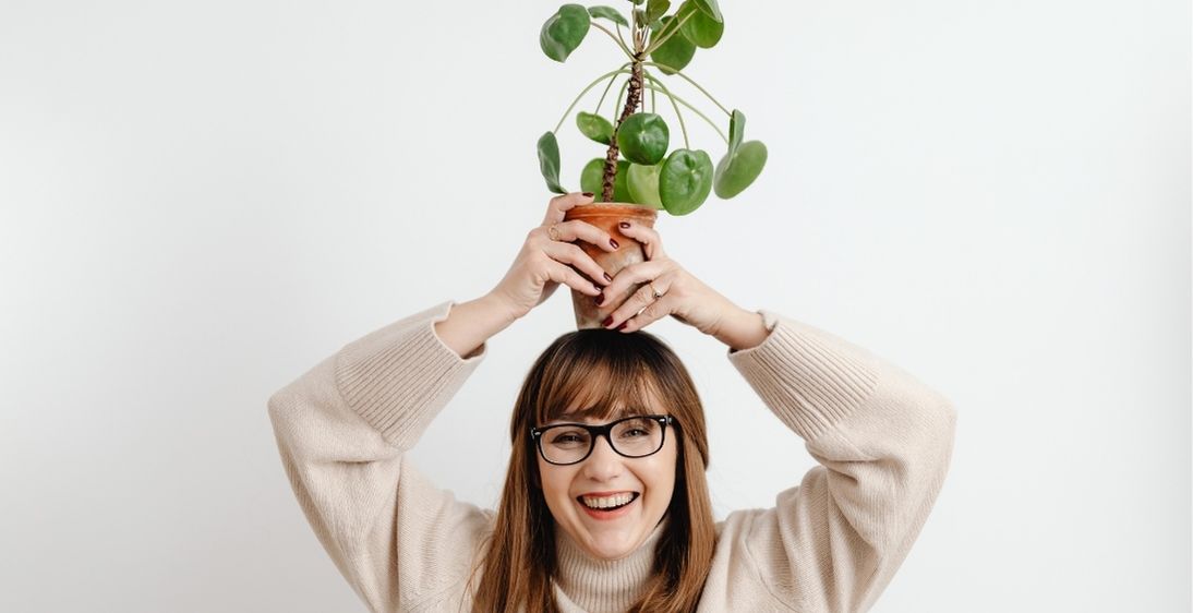 Person holding a potted plant above their head with a white background
